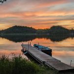 Gorgeous orange and yellow sunset over a lake with a long wooden dock and rowboat with light blue interior on Fish Trap Lake at Sams Island